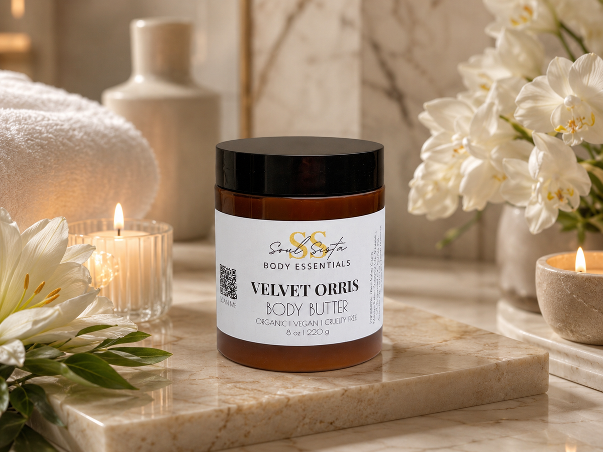 Soulsistabodyessentials Velvet Orris body butter jar on marble surface with candles and white flowers in background.